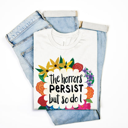 White t-shirt with colorful floral design and text on a pair of light blue jeans against a white background