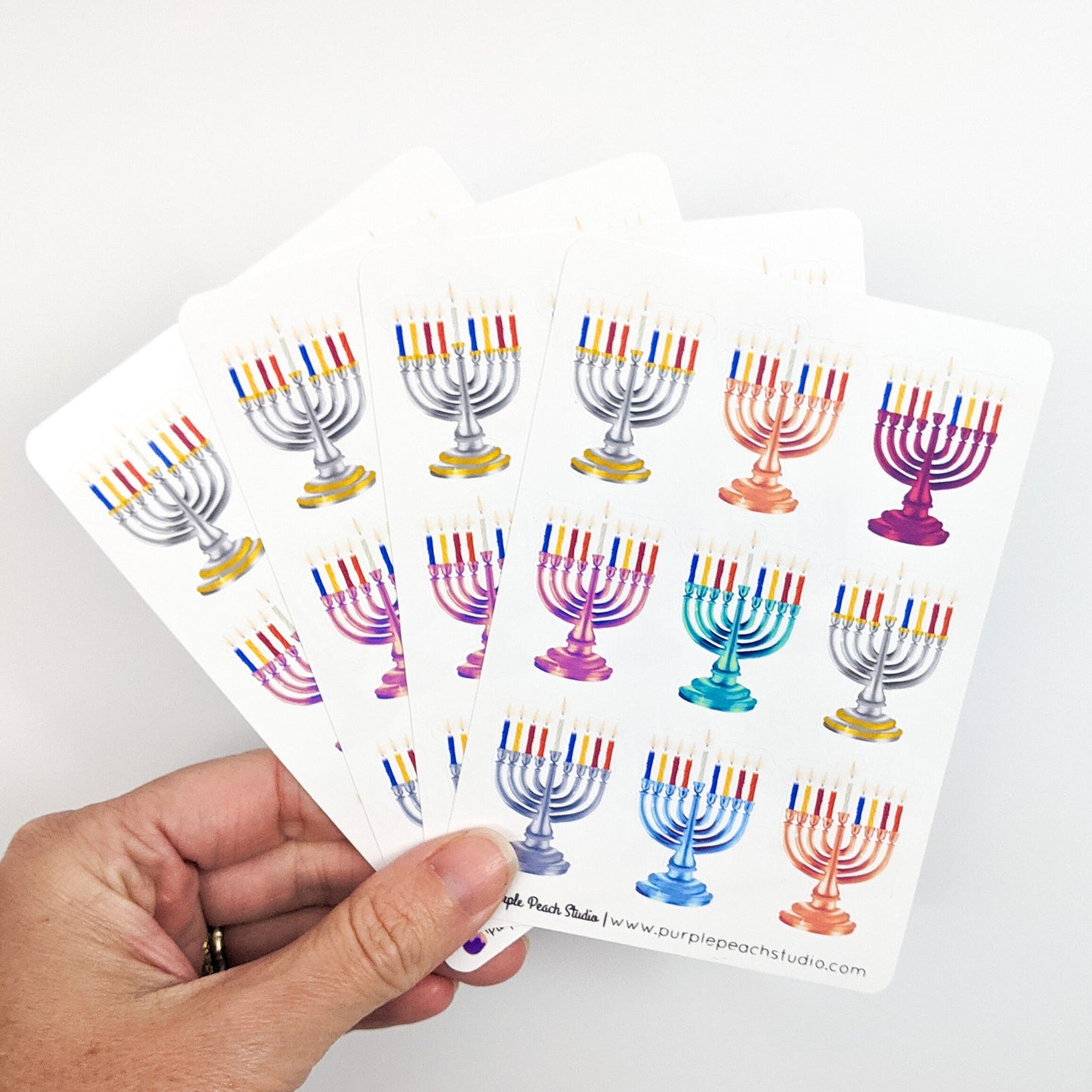 Sheet of colorful Menorah stickers held by a hand on a white background