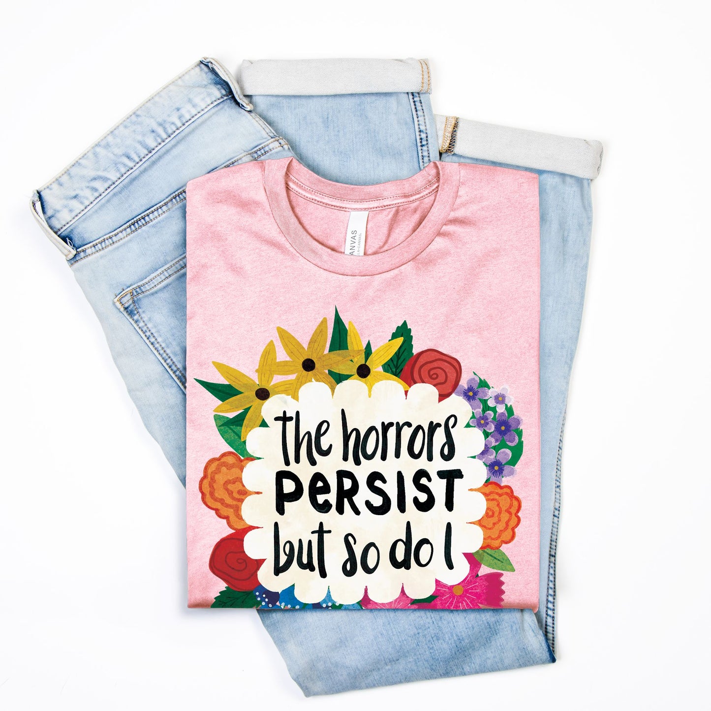 Pink t-shirt with floral design and text on top of denim jeans on a white background