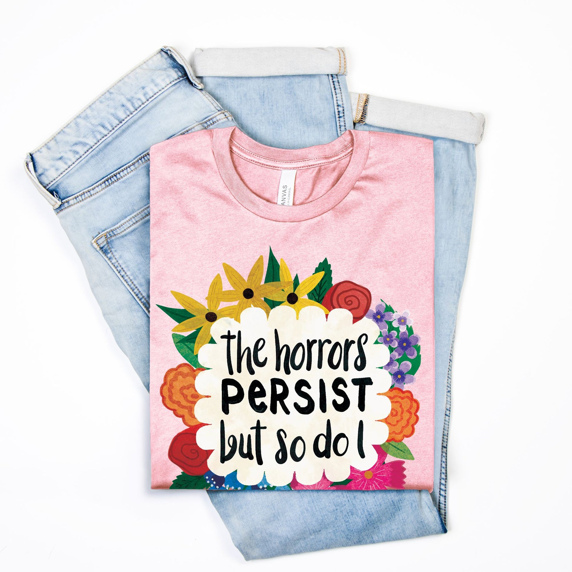 Pink t-shirt with floral design and text on top of denim jeans on a white background