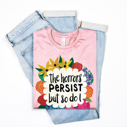 Pink t-shirt with floral design and text on top of denim jeans on a white background
